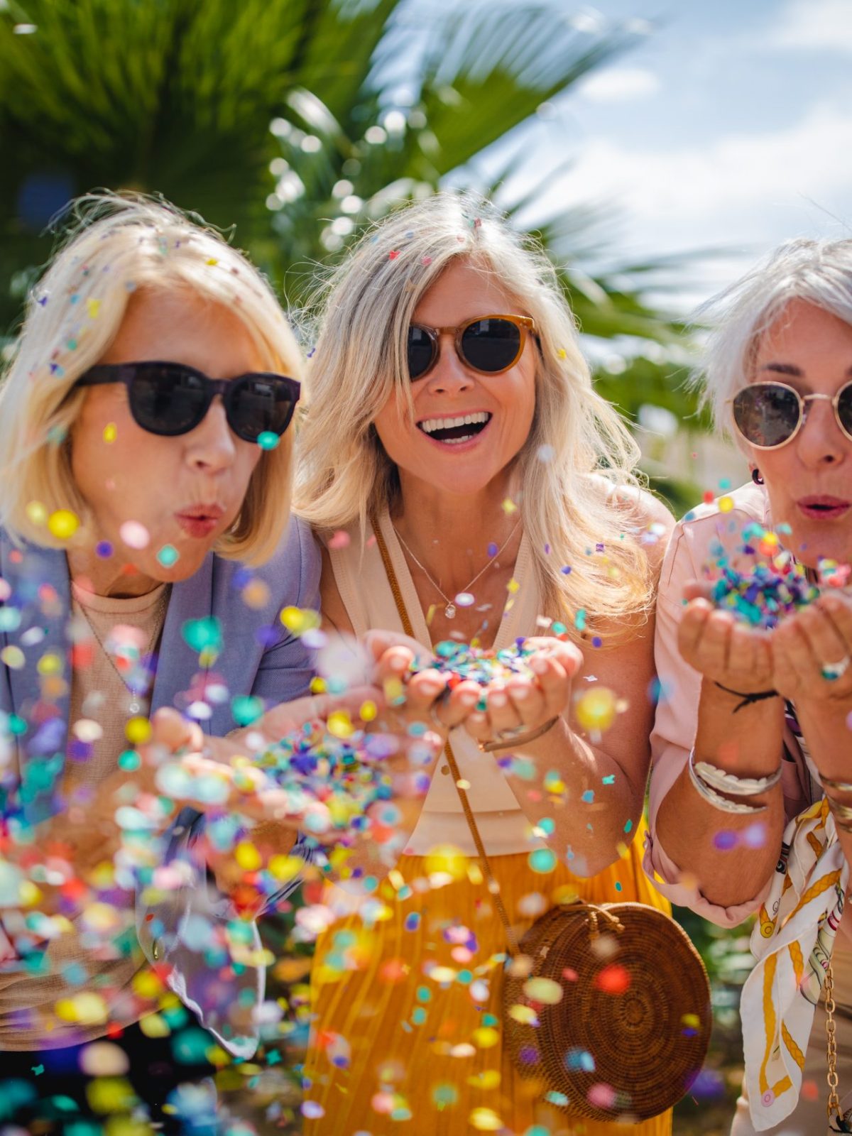 Fashionable mature friends having fun and celebrating by blowing colorful confetti in city street